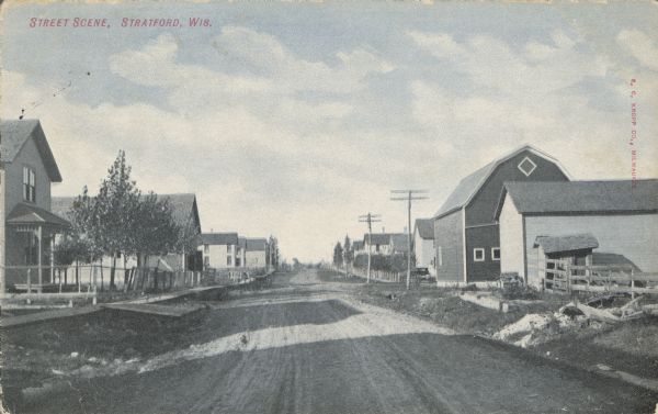 Text on front reads: "Street Scene, Stratford, Wis." An unpaved street with boardwalks and dwellings on the left, more dwellings and farm buildings on the right.