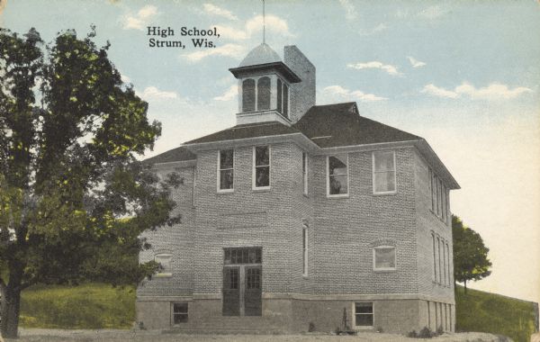Text on front reads: "High School, Strum, Wis." A two-story brick high school building with a belfry. There is a hill behind it with trees.