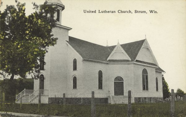 Text on front reads: "United Lutheran Church. Strum, Wis." A clapboard church with gable decorations and a belfry. A fence surrounds the church with a cemetery and trees.