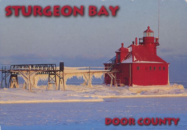 Text on front reads: "Sturgeon Bay, Door County." On reverse: "Sturgeon Bay, Wisconsin, Door County. North Pierhead Light. Winter shows its pretty face on the Sturgeon Bay ship canal which is the connecting link between Sturgeon Bay and Lake Michigan." Rime ice coats the pier that leads out to the lighthouse. Built in 1903, it is located on the north pier of the southern entrance to the Sturgeon Bay Ship Canal.
