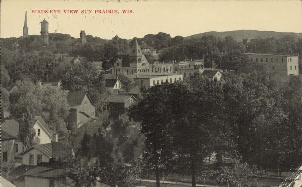 Text on front reads: "Bird's Eye View of Sun Prairie, Wis." An elevated view of dwellings, businesses among trees, with City Hall in the center. On the horizon are trees, buildings and hills.