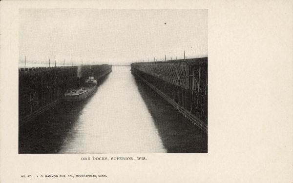 Text on front reads: "Ore Docks, Superior, Wis." Elevated view of an ore carrying ship that is within the ore docks on Lake Superior.