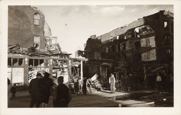 A crowd of people view the aftermath of a fire that destroyed the four story brick Hotel Superior and a dozen stores and offices. Nine fire companies attempted to stop the blaze. A sign on the left reads: "Coffee Shop." A barber pole is on the right.