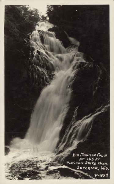 Text on front reads: "Big Manitou Falls, Ht. 165 Ft., Pattison State Park, Superior, Wis." The falls are on the Black River and surrounded by shrubs and rocks.