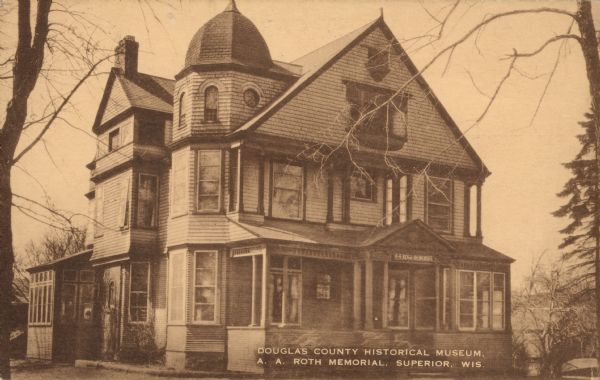 Text on front reads: "Douglas County Historical Museum, A.A. Roth Memorial, Superior, Wis." This home housed the Douglas County Museum from 1939 to 1963. They were offered the home of the A. A. Roth family to use as their museum in 1938. Alois Roth was a partner with his brother Theodore in the Roth Brothers Department Store in Superior.