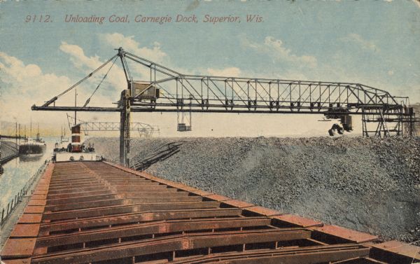 Text on front reads: "Unloading Coal, Carnegie Dock, Superior, Wis." A Great Lakes freighter is being unloaded by a gantry crane at a dock. An enormous pile of coal is on the right. Other ships and cranes are in the distance.