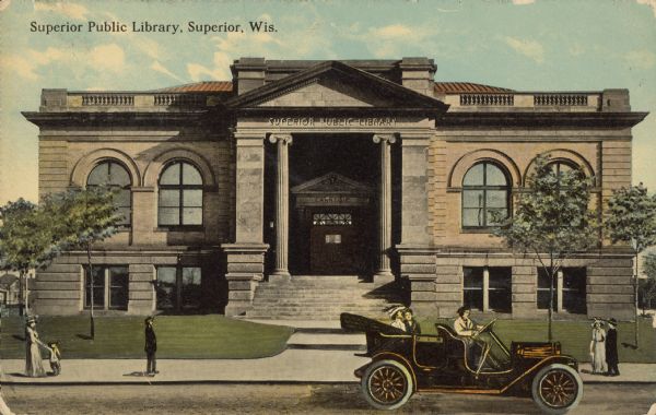 Text on front reads: "Superior Public Library, Superior, Wis." A Carnegie Library, built in 1902 of brick in the Neoclassical style. It was the oldest Carnegie Library built in Wisconsin. An automobile is parked at the curb and pedestrians are on the sidewalk.
