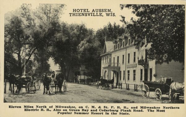 Text on front reads: "Hotel Aussem, Thiensville, Wis. Eleven Miles North of Milwaukee, on C.M. & St. P.R.R., and Milwaukee Northern Electric R.R., Also on Green Bay and Cedarburg Plank Road. The Most Popular Summer Resort in the State." Originally the Memmler Hotel, Fred and Maria Memmler sold the hotel to Gerhard Aussem in 1911. He changed the name and it remained the Aussem Hotel until 1947. Many horse-drawn wagons are in the unpaved street in front of the hotel, and another building is beyond it. Several men are in or near their wagons. Trees surround the hotel.