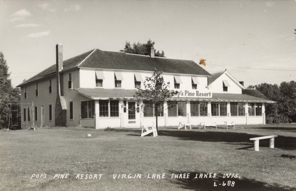 Text on front reads: Pop's Pine Resort, Virgin Lake, Three Lakes, Wis." A large clapboard building with many windows and a long enclosed porch. There is lawn furniture in front and a swing set on the left. Trees are in the background.