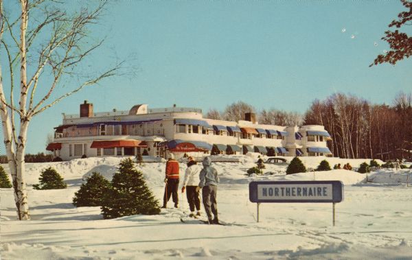 Text on reverse reads: "Northernaire, Three Lakes, Wisconsin. Open Year 'Round." View of Northernaire Resort, on Deer Lake, an Art Moderne hotel built in 1946. Three skiers are on the snow-covered ground, gazing at the white resort building with blue and red awnings. Another group of people are in the background on the right. A large sign reads: "Northernaire." Trees are behind the hotel.