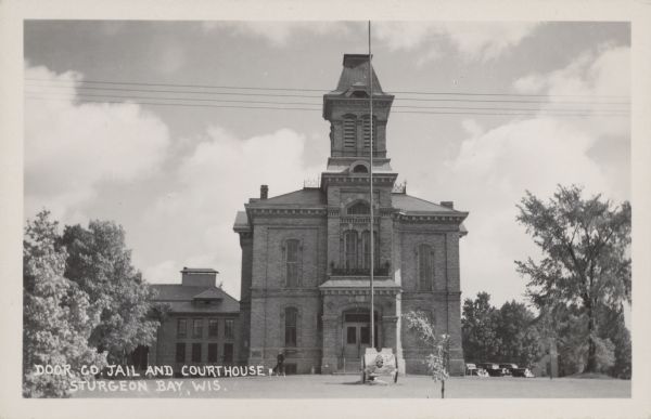 Text on front reads: "Door Co. Jail and Courthouse. Sturgeon Bay, Wis."
The second courthouse built in 1878 of brick in the Italianate style. There is a woman on the sidewalk and a cannon on the lawn. The current courthouse was built as an addition and the original building was demolished in 1991.