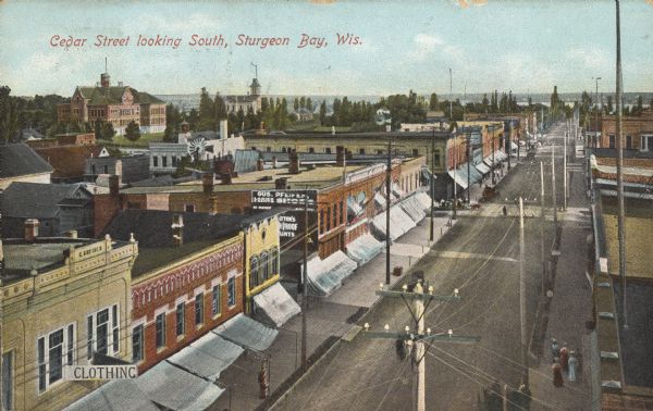 Text on front reads: "Cedar Street looking South, Sturgeon Bay, Wis." Elevated view of storefronts on a street, the west facing stores all have awnings. A sign on the store on the left reads: "Clothing" and a wall sign reads: "Gus. Pfeifer Ladies & Gents Shoes." Pedestrians are on the sidewalks. Sturgeon Bay is on the horizon. Cedar Street was renamed 3rd Avenue during WWII.