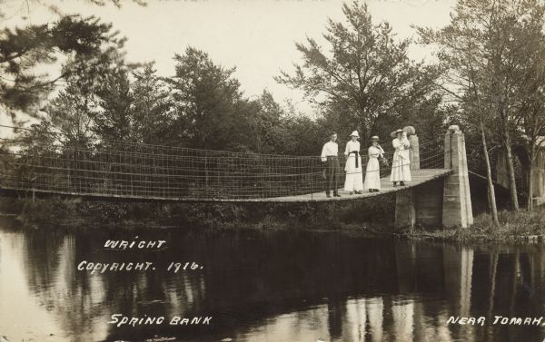 Text on front reads: "Spring Bank, Near Tomah." Three women and a man stand on a wooden suspension bridge over a pond on Sparta Creek. One woman is holding a baby.
