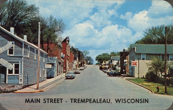 Text on front reads: "Main Street - Trempealeau, Wisconsin." On reverse: "On the Grand Old Mississippi and the Great River Road near Perrot State Park and Lock and Dam No. 6. Known as the 'Garden of Eden' and for its Scenic Beauty. Hunting - Fishing - Boating - Cottages - 'A Sportsman's Paradise' - Modern Grade and High School - Three Churches. A Growing Community and a Fine Place to Live. 'We Like It Here.'" View up Main street lined with businesses.