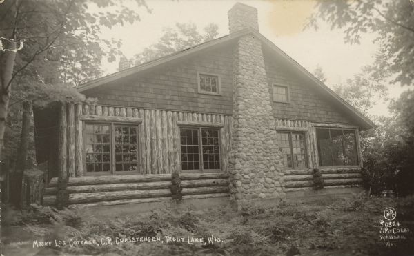Text on front reads: "Musky Log Cottage, C.P. Christensen, Trout Lake, Wis." A log cabin with large windows, a screened porch and a rubble stone chimney. It is surrounded by trees. Trout Lake is located between Boulder Junction and Arbor Vitae, Wisconsin.