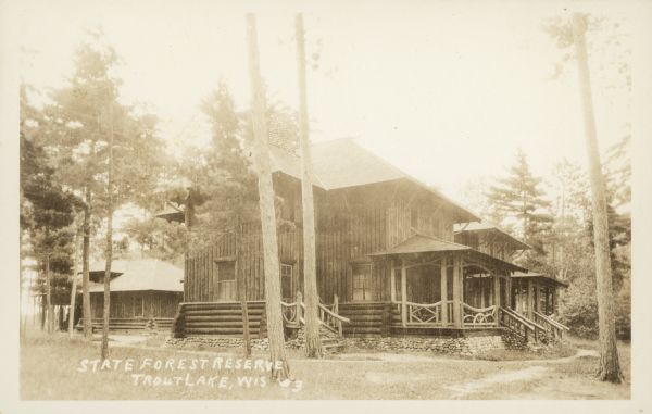 Text on front reads: "State Forest Reserve, Trout Lake, Wis." A two-story log building with a rubble stone foundation. The porch and stairs have ornate pine log railings. Another building is in the background on the left.<p>For more information, see the Image Gallery Essay: "Life at the State House: Trout Lake Forestry Headquarters" on the Wisconsin Historical Society website.</p>