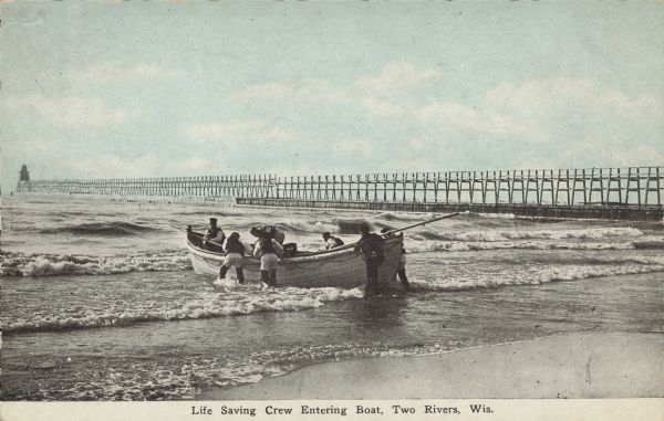 Text on front reads: "Life Saving Crew Entering Boat, Two Rivers, Wis." A group of men launching a large rowboat into Lake Michigan. In the background is a long pier with a lighthouse or beacon at the end.