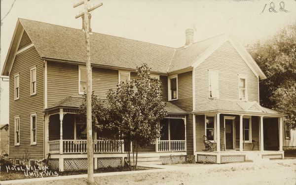 Caption reads: "Hotel Nelson, Unity, Wis." A two-story clapboard dwelling with two porches. There are trees in front and to the right.