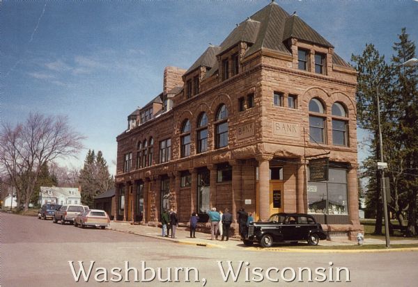 Text on front reads: "Washburn, Wisconsin." On reverse: "Washburn Historical Museum and Cultural Center. National Register of Historical Places. Washburn, Wisconsin." A group of pedestrians stand on the sidewalk near the entrance of the Cultural Center, and an antique automobile is parked in front on the sidewalk. More cars are parked on the left with dwellings and trees in the distance. This building was originally the Bank of Washburn, built in 1890 of brownstone in the Richardson Romanesque style. Restoration of the building began in 1991 and a celebration marked the grand opening of the Washburn Cultural Center in 1993.