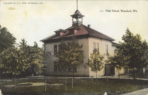 Text on front reads: "High School, Waterford, Wis." A brick, two-story high school with a belfry, surrounded by trees.