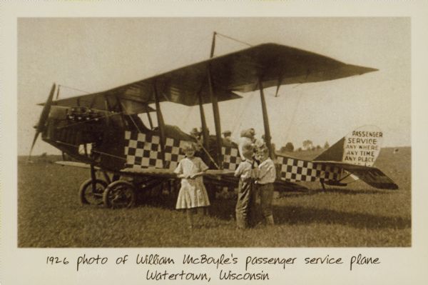 Text on front reads: "1926 photo of William McBoyle's passenger service plane, Watertown, Wisconsin." On reverse: "Front: 1926 photo of William McBoyle's passenger service plane. Back: A Cessna citation Executive Jet owned by Wisconsin Aviation as part of its air charter fleet." Three children are standing in front of William McBoyle's passenger service plane, a group of adults are standing behind it. Text on the tail reads: "Passenger Service, Any Where, Any Time, Any Place." On the reverse is a ghosted image of Wisconsin Aviation. Wisconsin Aviation operates the Watertown Municipal airport for the city and offers a wide variety of aviation services to include flight training. Visit www.wisconsinaviation.com for other services and events."