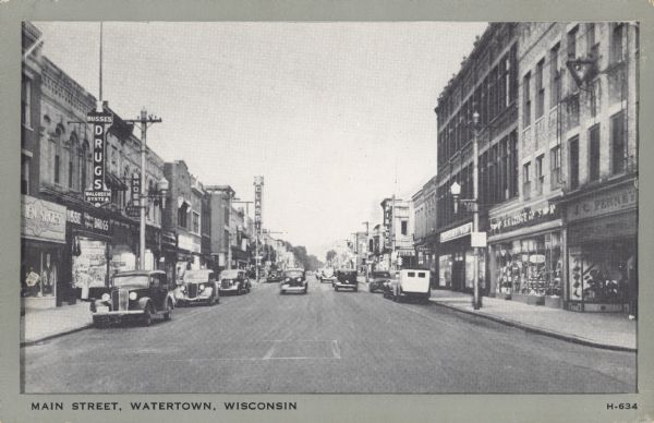 Text on front reads: "Main Street, Watertown, Wisconsin." A busy street scene with automobiles in the street and parked along the curb. The street is lined with many businesses, display windows and sidewalks. Signs read: "Busses Drugs Walgreen System", "Shoes", "Fields", "J.C. Penney", "S.S. Kreske" and "Classic."