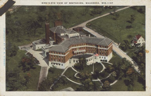 Text on front reads: "Bird's-Eye View of Resthaven, Waukesha, Wis." Built in 1905 of brick in the Neoclassical style, Resthaven was a large resort hotel from the Springs Era in Waukesha. It was meant as a hotel for the overworked to restore their health, but only lasted until 1919 when it was sold to the Veterans Administration as a recuperative hospital and later a tuberculosis hospital. It was closed in 1958 and after several years purchased by the New Tribes Bible Institute.