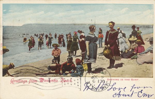 Text on front reads: "Greetings from Waukesha Beach. Bathing in the Surf." Children and adults wear Victorian bathing suits as well as regular clothing on the beach and in the water, many with hats. The far shore is visible on the horizon. Waukesha Beach is located on Pewaukee Lake.