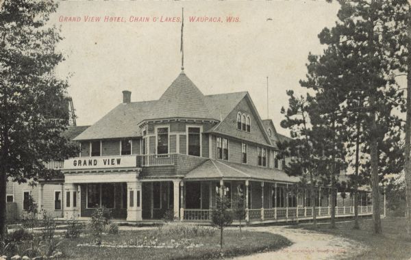 Text on front reads: "Grand View Hotel, Chain O' Lakes, Waupaca, Wis." The two story hotel was located on Rainbow Lake and opened in 1894. It had a 16 foot wide porch on three sides. A sign on the railing of the balcony reads "Grand View." In 1945 the property was purchased by the State of Wisconsin and the buildings were razed in 1946.