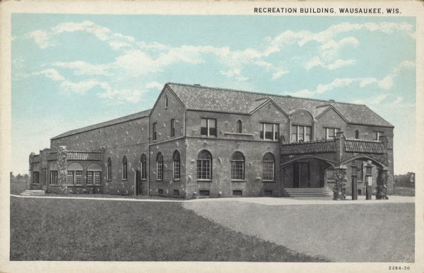 Text on front reads: "Recreation Building, Wausaukee, Wis." A two-story, brick and stone building with a portico, gasoline pumps and arched windows.