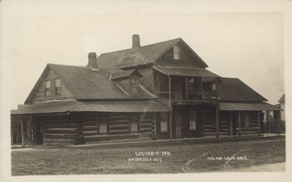 Text on front reads: "Log-Cabin-Inn, Wausaukee-Wis." A two-story inn built of logs with a covered porch, balcony, and dormer windows.