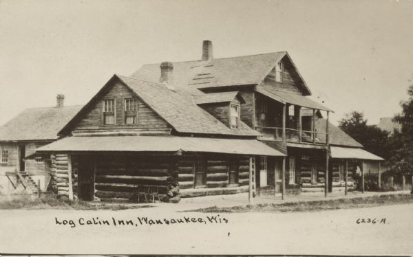 Text on front reads: "Log Cabin Inn, Wausaukee, Wis." A two-story inn built of logs with a covered porch, balcony, and dormer windows.