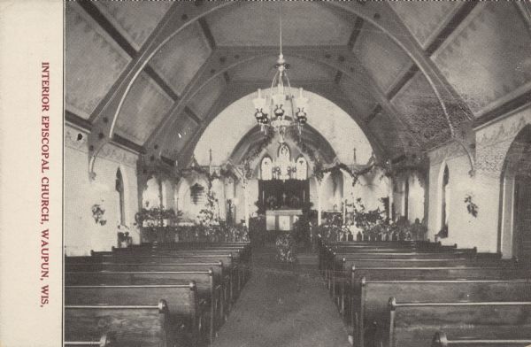 Text on front reads: "Interior Episcopal Church, Waupun, Wis." Trinity Episcopal Church was built in 1871. Interior view with wooden pews, chandelier, ornate altar and vaulted ceiling. Foliage is used as a decoration. The same congregation has occupied the church since its founding.