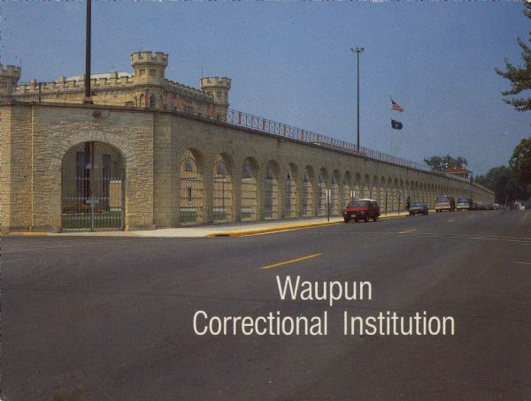 Text on front reads: "Waupun Correctional Institution." On reverse: "Waupun Correctional Institution. Located two blocks from Main Street on Madison Street, it is a state prison for convicted male felons. The site was selected by a prison commission appointed by the Wisconsin Legislature in 1851." The outer wall of the prison, built of limestone with wrought iron gate and grills. The original Gothic Revival main building can be seen inside. Cars are parked at the curb.