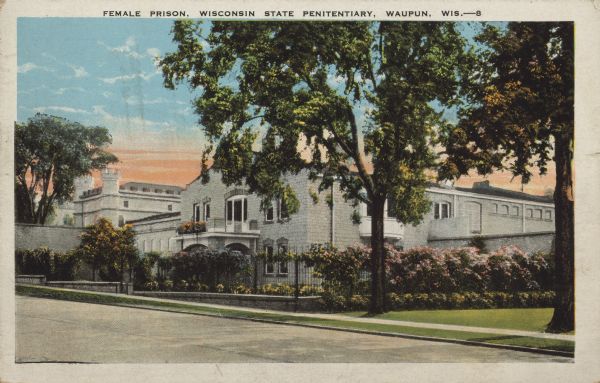 Text on front reads: "Female Prison, Wisconsin State Penitentiary, Waupun, Wis." A building that housed female prisoners surrounded by trees, fences and gardens. The towers of the main building can be seen in the background on the left.
