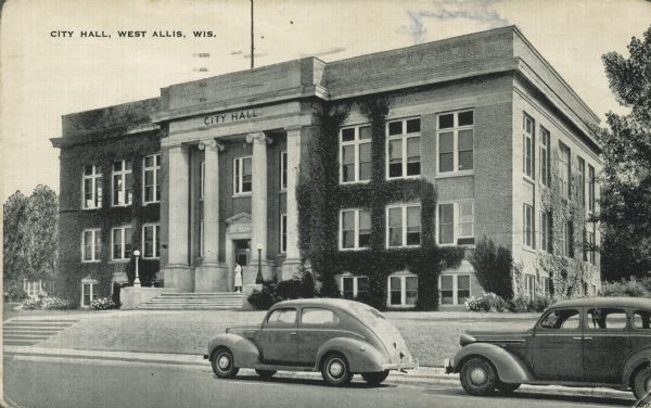 Text on front reads: "City Hall, West Allis, Wis." The entrance is two stories and has four columns, and the building is partially covered with vines. A woman is standing at the front door and automobiles are parked at the curb. Built in 1921, it was demolished and replaced by a new City Hall in 1970.