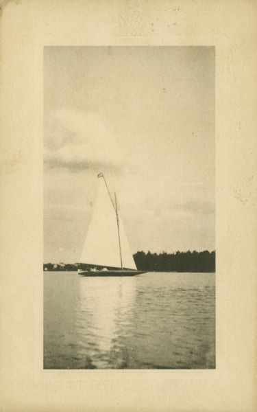 A sailboat on a lake with a wooded shoreline in the distance.
