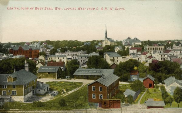 Text on front reads: "Central View of West Bend, Wis., Looking West from C. & N. W. Depot." An elevated view of the city with railroad tracks in the foreground. A sign on two roofs reads: "Wallau Dairy Co."
