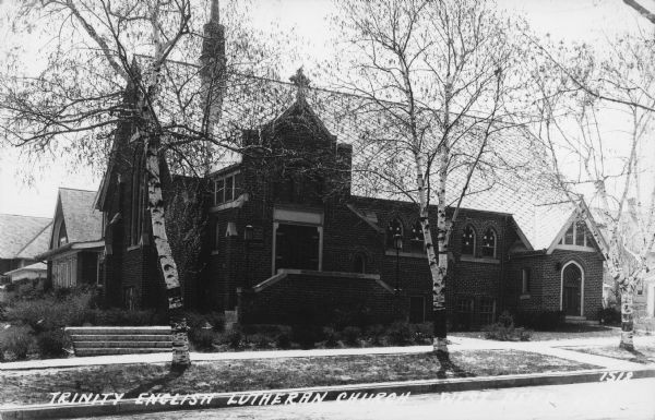 Text on front reads: "Trinity English Lutheran Church, West Bend, Wis." View from street of the brick, Gothic Revival church built in 1926.