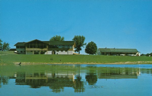 Text on reverse: "West Bend Country Club, West Bend, Wisconsin." Two buildings, trees and a pond at the West Bend Country Club. The front nine opened in 1930 and the back nine opened in 1960.