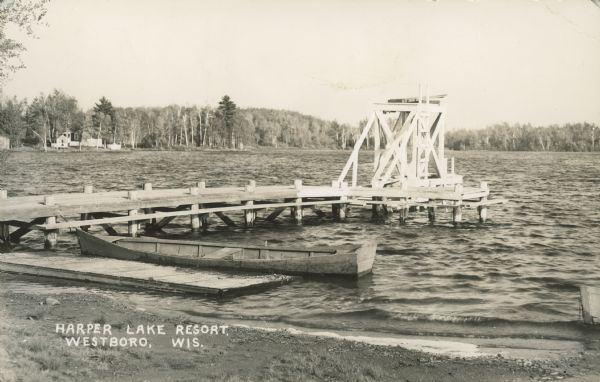 Text on front reads: "Harper Lake Resort, Westboro, Wis." Swimming dock with a ladder leading up to a diving platrom on Harper Lake. A rowboat is moored to another dock parallel to the shore. A group of buildings are along the far shoreline on the lefte. Handwritten on the reverse: "View of Harper's Lake. My cottage and our bldgs [<i>sic</i>] on the point across from the swimming dock." North Harper Lake and South Harper Lake are located east of Westboro.