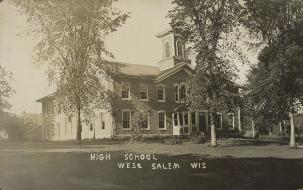 Text on front reads: "High School, West Salem, Wis." A two-story, brick high school with arched windows and a belfry. It is surrounded by a lawn and trees.