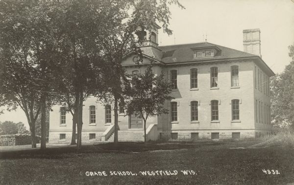 Text on front reads: "Grade School, Westfield, Wis." Originally built in 1887, the grade school students were downstairs and the high school students upstairs. A two-story, brick building, with an attic and basement, surrounded by trees and a lawn.In 1904, the size was doubled with an extension. In 1922, it became solely an elementary school when a new high school was built. A new elementary school was built in 1968.