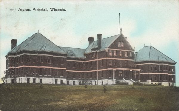 Text on front reads: "Asylum, Whitehall, Wisconsin." A multi-story building with a full basement and attic surrounded by a large lawn with small trees. Built of brick in the Romanesque Revival style in 1899. The original name was "Trempealeau County Asylum and Poor House Farm," changed in 1947 to "Trempealeau County Hospital" and finally to "Trempealeau County Health Care Center" in 1974. A hospital addition was built in 1969, after which the original building was demolished. 