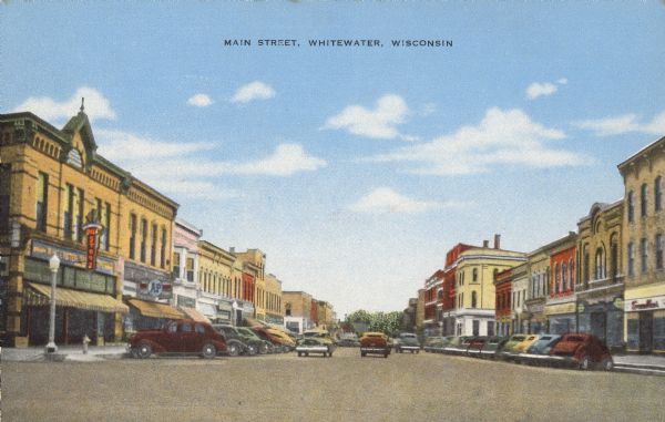 Text on front reads: "Main Street, Whitewater, Wisconsin." The downtown area with buildings, storefronts and sidewalks along Main Street. Automobiles are on the street and parked diagonally.