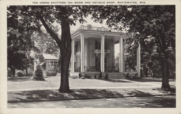 Text on front reads: "The Green Shutters Tea Room and Antique Shop, Whitewater Wis." The brick, Italianate style building surrounded by a lawn, trees and shrubs was built in 1841. From the Property Record on the Wisconsin Historical Society website: "This Greek Revival house was built in 1860 by Mr. Parker and later sold to Jacob Starin. This was the site of the first Sunday School in Whitewater in 1841. The house was remodeled in 1912 and 1924. In 1920, the fanlight-topped French doors and large veranda were added by owner, Sander Hoyum. The first floor was once an elegant restaurant — The Green Shutters. Today it is a professional office." It is listed on the State and National Register of Historic Places.