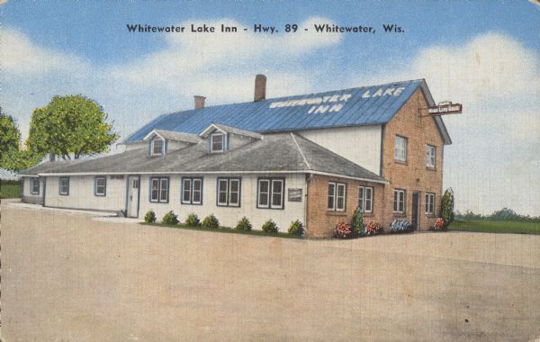 Text on front reads: "Whitewater Lake Inn - Hwy. 89 - Whitewater, Wis." On reverse: "Whitewater Lake Inn. Excellent Food - Steaks - Chicken - Sea Foods. Cocktail Bar. Dancing Every Saturday. Open Year Round. Located on Hwy. 89 - 5 1/2 miles south of Whitewater, Wis. - Ben & Alma Noltner." The building has "Whitewater Lake Inn" painted on the roof and a "Miller High Life" sign above the door. A large parking area surrounds two sides of the building.