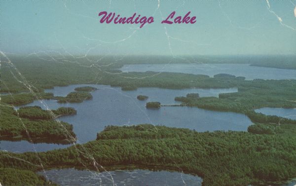 Text on front reads: "Windigo Lake." On reverse: "Windigo Lake. 7 miles South of Hayward, Wisc. on Hiway 27. Vacation Paradise of Northern Wisconsin." Aerial photograph of Lake Windigo with the surrounding lakes and forests.