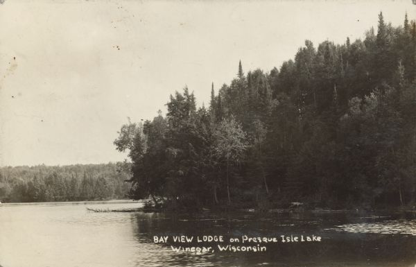 Text on front reads: "Bay View Lodge on Presque Isle Lake, Winegar, Wisconsin." A forested point of land jutting into Presque Isle Lake. The far shore is in the distance. In 1905, J.J. Foster built a lumber mill and named the town Foster. In 1910, William S. Winegar bought the mill and renamed the town Winegar. Finally, in 1959, the town was renamed Presque Isle.