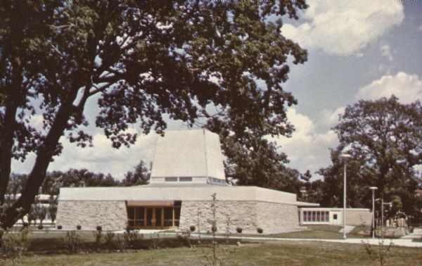 Text on reverse reads: "All Faiths Chapel. Winnebago State Hospital. Winnebago, Wisconsin. Completed in 1969. In addition to the main chapel, which seats 200, it has two smaller chapels, offices for the hospital chaplain's and several meeting rooms. This chapel was used by all faiths." Additional text on a sticker on the reverse reads: "Friends of Julaine Farrow Museum. To establish and develop effective community partnerships and promote awareness of the Julaine Farrow Museum; Located on the grounds of Winnebago Mental Health Institute. The friends will assist with working with museum archives and artifacts; communicating and promoting the museum within their communities, while supporting WMHI, its mission, its past, and its current needs. The friends will assist in coordination the efforts of groups and individuals interested in the welfare of historic preservation." The chapel is surrounded by a lawn and trees.